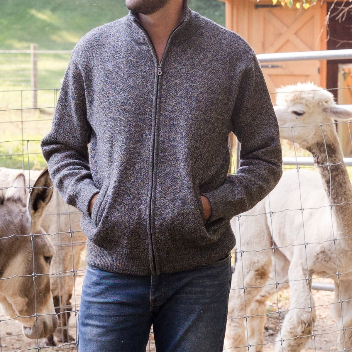 Men's Heavyweight Full-Zip Baby Alpaca Wool Jacket – A man wearing a marled black and white knitted baby alpaca wool zip jacket stands in front of an animal enclosure.