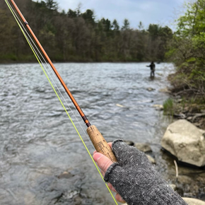 Grey alpaca gloves worn by man fishing in front of river.