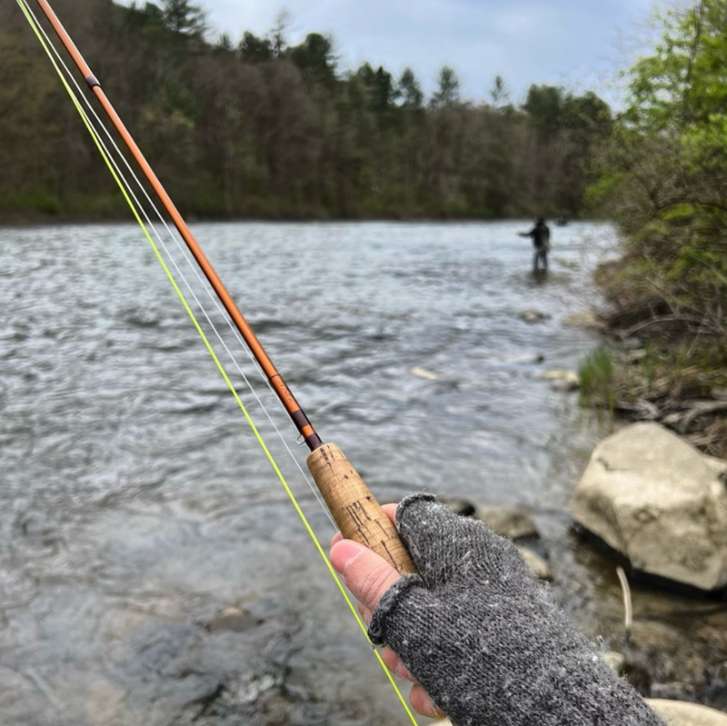 Grey alpaca gloves worn by man fishing in front of river.