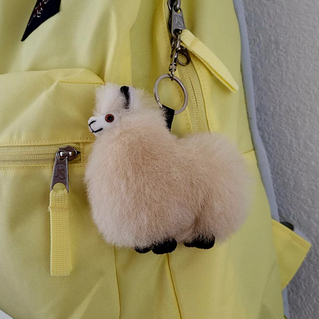 A plush tan alpaca keychain attached to a yellow backpack zipper.