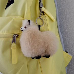 A plush tan alpaca keychain attached to a yellow backpack zipper.