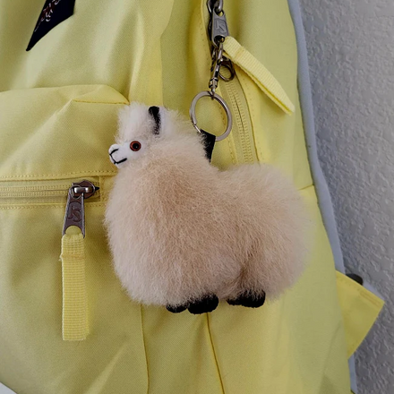 A plush tan alpaca keychain attached to a yellow backpack zipper.