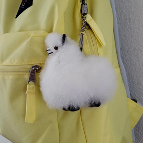 A plush white alpaca keychain attached to a yellow backpack zipper.