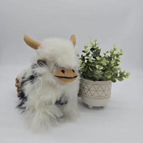 Plush toy yak next to a small potted plant on a light gray background