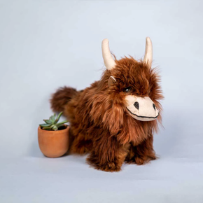 Plush toy Highland cow next to a small potted plant on a light gray background