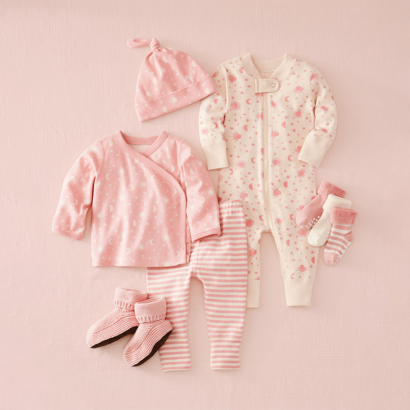 Collection of baby clothing including a pink outfit, onesie, hat, and socks on a pink background