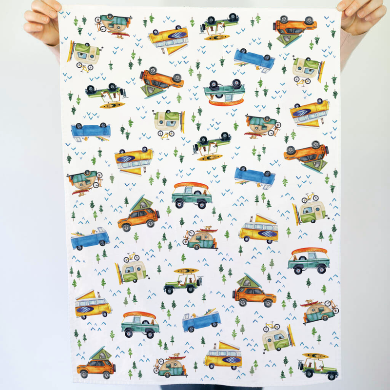 Tea towel with colorful vehicle pattern held by two hands against a white background