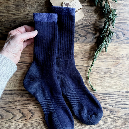 Navy blue socks held by a hand on a wooden surface with a branch.
