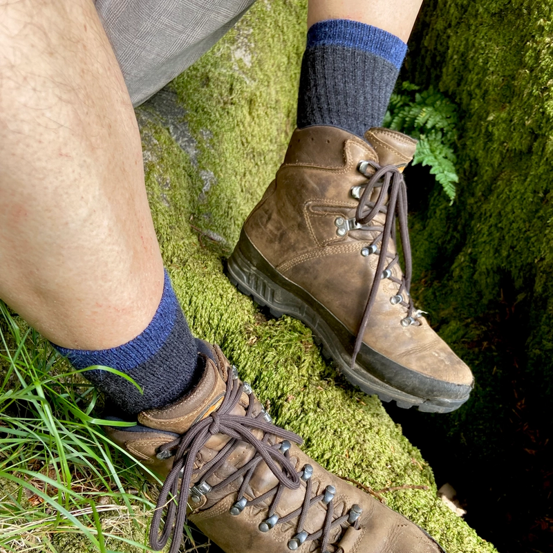 Brown hiking boots with blue & black socks on a green mossy surface