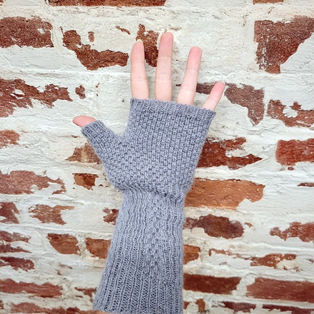 Gray fingerless glove on a hand against a textured brick wall background