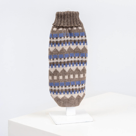 A dog sweater with a geometric pattern featuring earthy hues and a tranquil blue, displayed on a white platform.