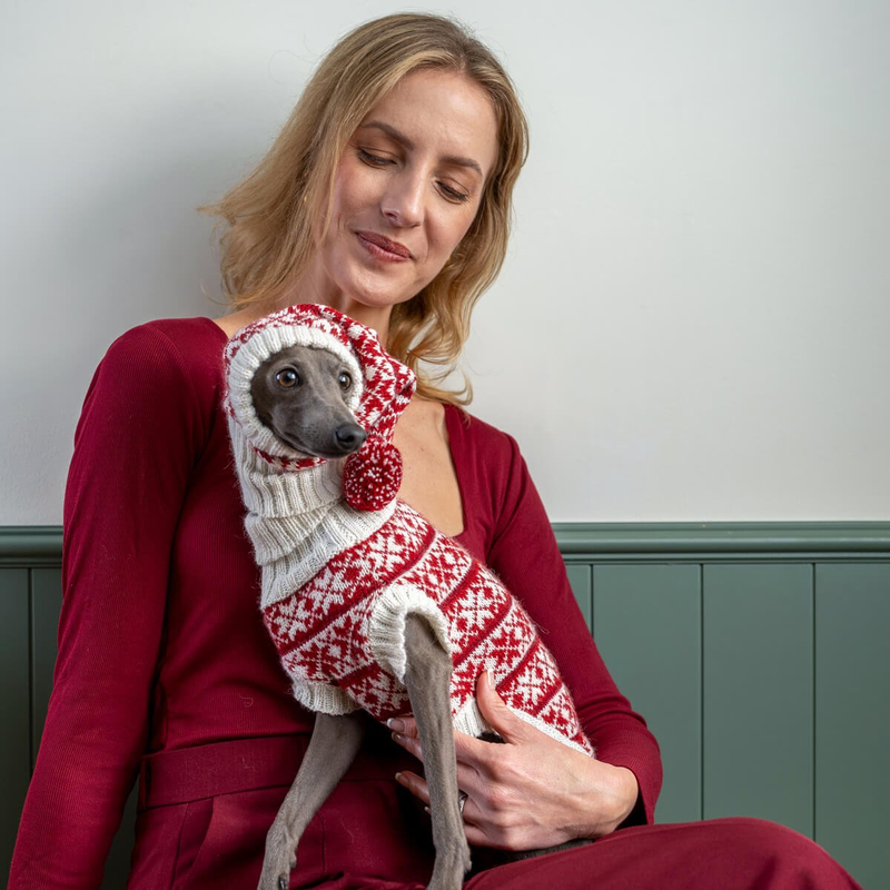 Woman holding a dog wearing a red and white patterned sweater against a plain background