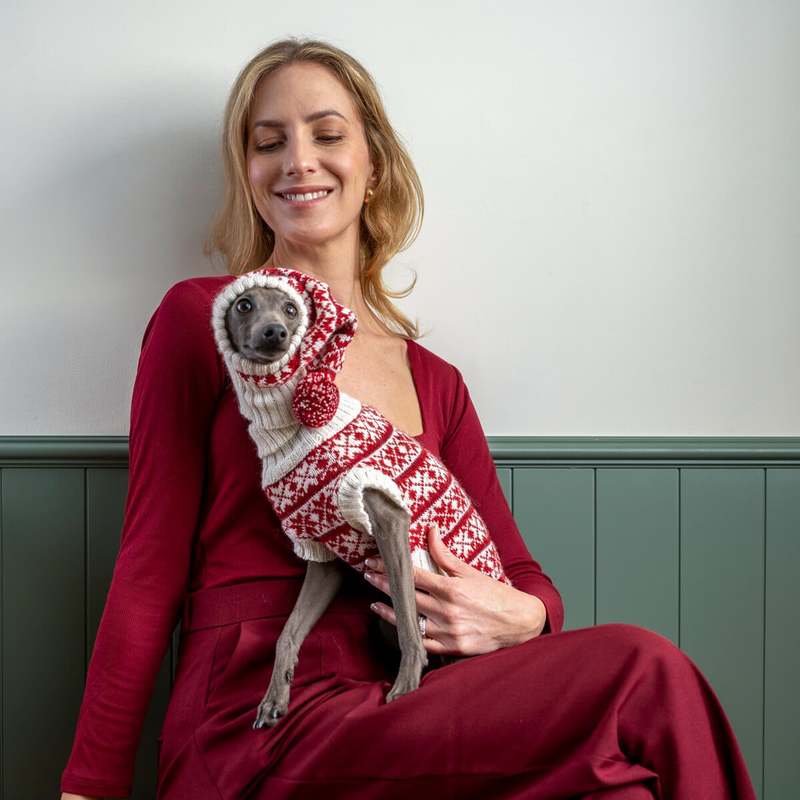 Woman holding a small dog wearing a red and white sweater against a plain background