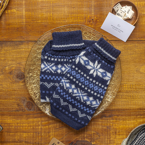 Blue knitted dog sweater with white patterns on a wooden surface