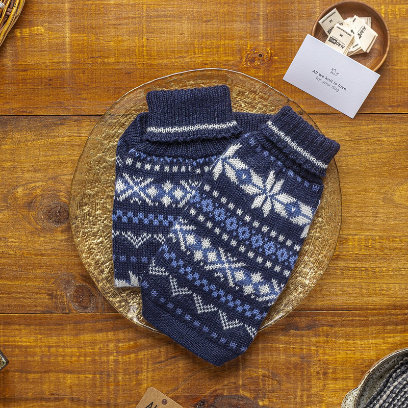 Blue knitted dog sweater with white patterns on a wooden surface
