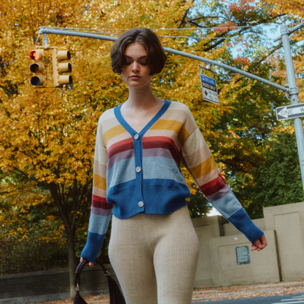 Woman wearing a colorful striped sweater on a city street with autumn trees.