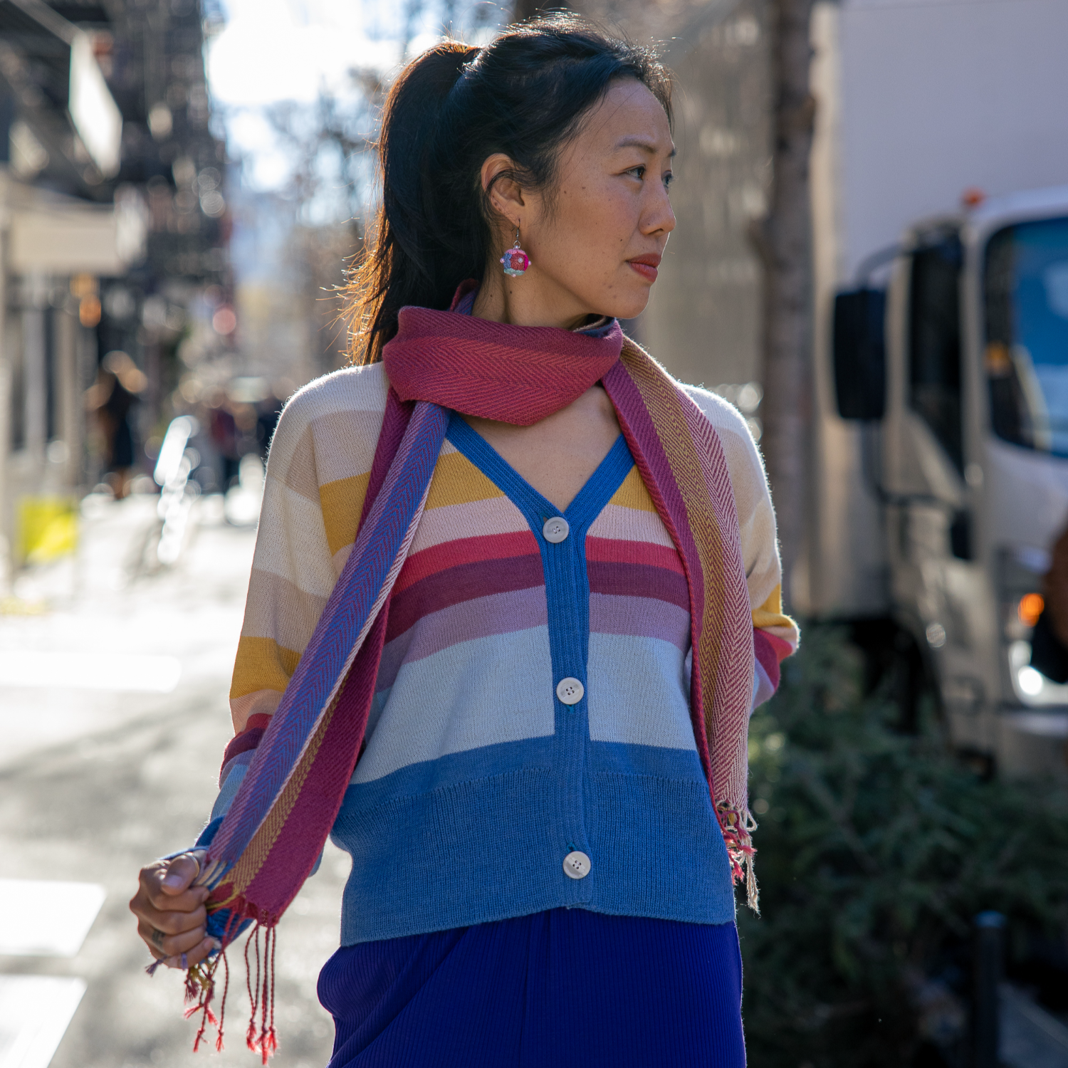 Woman wearing a colorful striped sweater and blue pants on a city street.
