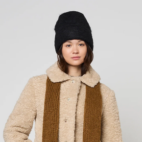 Person wearing a beige coat, brown scarf, and black beanie on a white background