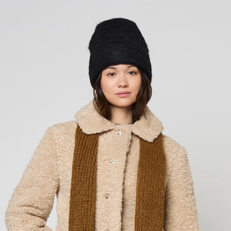 Person wearing a beige coat, brown scarf, and black beanie on a white background