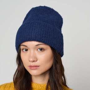 Woman wearing a blue knit beanie and yellow sweater against a plain background