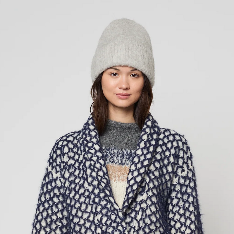 Person wearing a patterned coat, white skirt, and gray beanie on a plain background