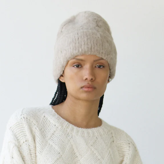 Person wearing a cream knitted sweater and hat against a white background