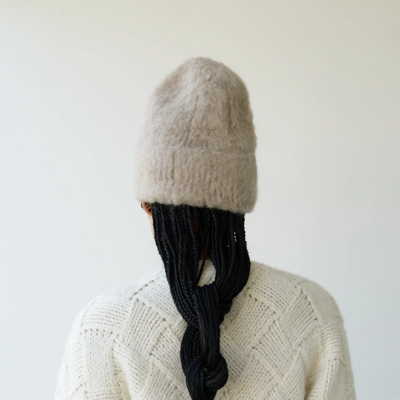 Person wearing a cream sweater and knit hat with a plain background