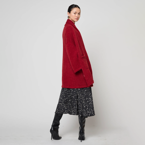 Woman wearing a red coat, black patterned skirt, and black boots on a white background