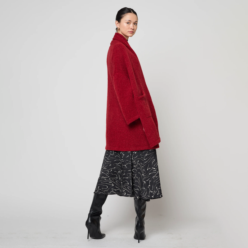 Woman wearing a red coat, black patterned skirt, and black boots on a white background
