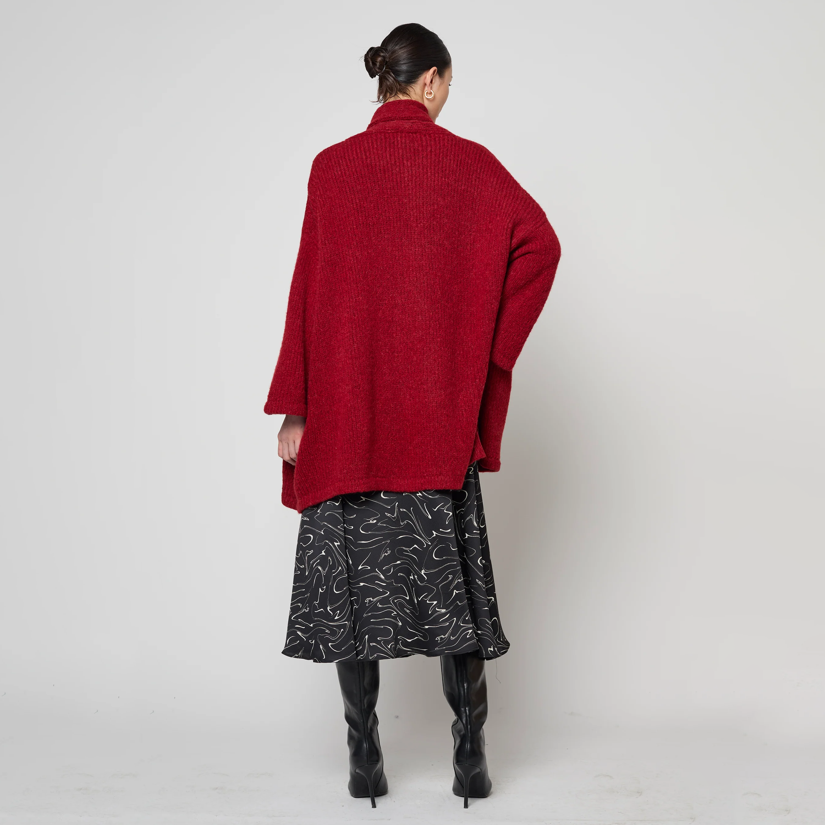Person wearing a red coat, black patterned skirt, and black boots on a white background