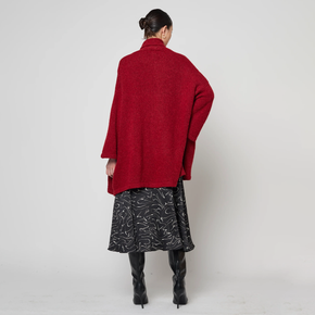 Person wearing a red coat, black patterned skirt, and black boots on a white background