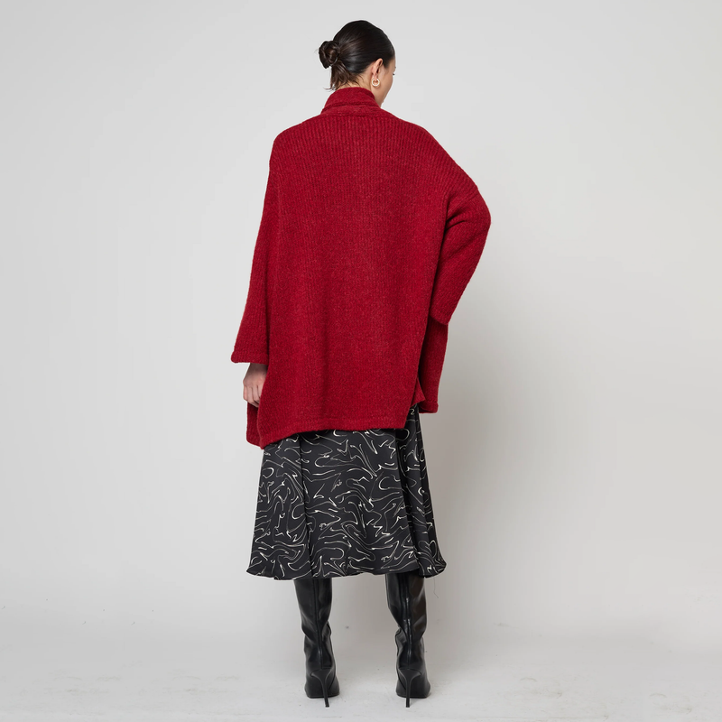 Person wearing a red coat, black patterned skirt, and black boots on a white background
