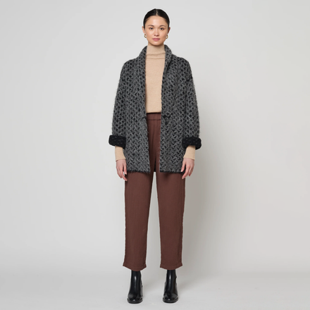 Woman wearing a patterned coat, beige sweater, and brown pants on a white background