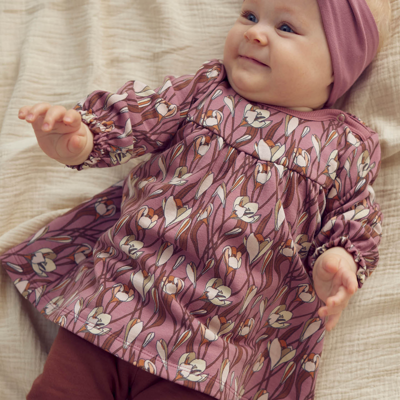 Baby wearing a pink floral dress and headband on a beige blanket