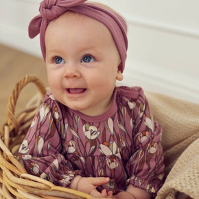 Baby wearing a pink floral outfit and turban sitting in a basket.