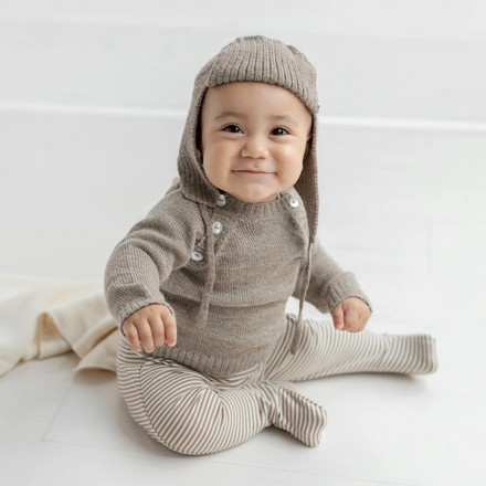 Baby wearing a knitted brown outfit with a hood on a white background
