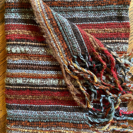 Scarf with multicolored stripes and fringes on a wooden surface
