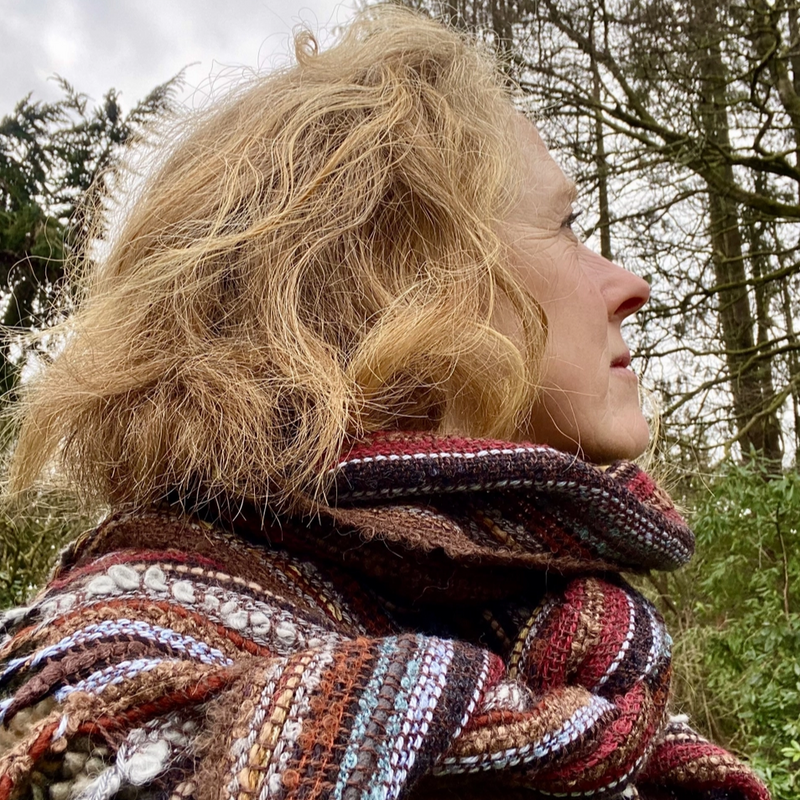 Person wearing a colorful scarf with a natural background of trees and sky.