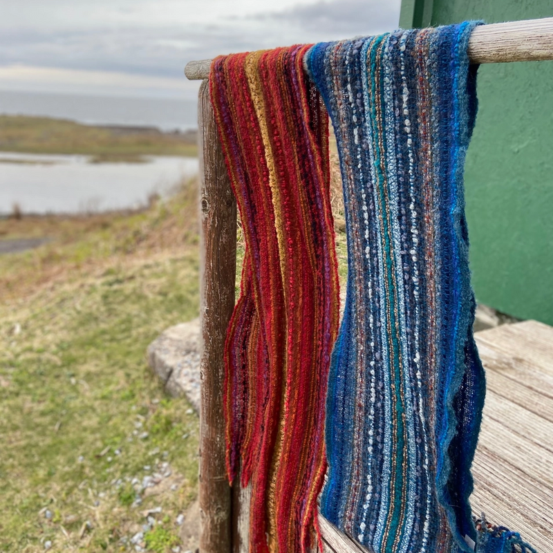 Colorful knitted scarves hanging on a railing with a scenic background