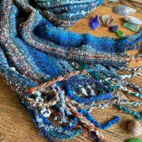 Textured blue scarf on a wooden surface with seashells and sea glass.