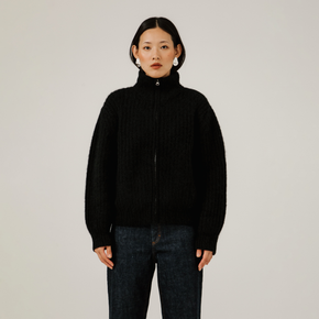 Person wearing a black turtleneck zip up rib knit sweater and dark jeans against a plain background