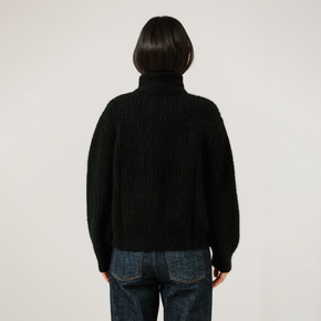 Person wearing a black turtleneck rib knit sweater and blue jeans on a plain background
