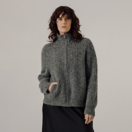 Woman wearing a gray zip up rib knit sweater against a plain background