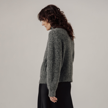 Woman wearing a gray rib knit jacket against a plain background
