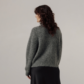 Woman wearing a gray rib knit sweater against a plain background