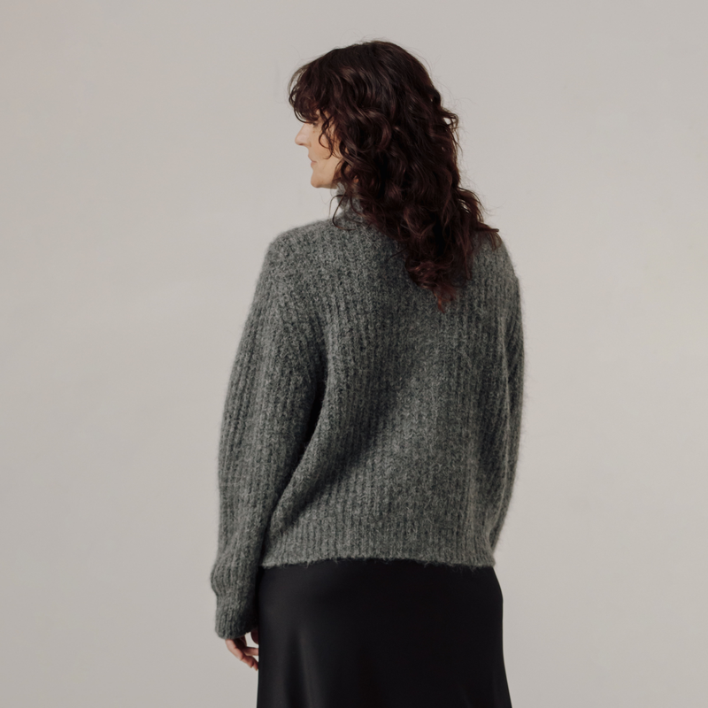 Woman wearing a gray rib knit sweater against a plain background