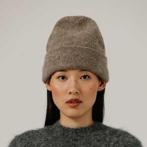 Person wearing a beige knit beanie and gray sweater against a plain background
