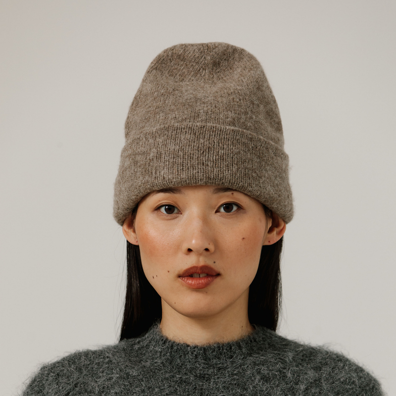 Person wearing a beige knit beanie and gray sweater against a plain background