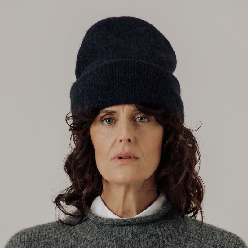 Woman wearing a dark blue knit beanie and gray sweater against a plain background