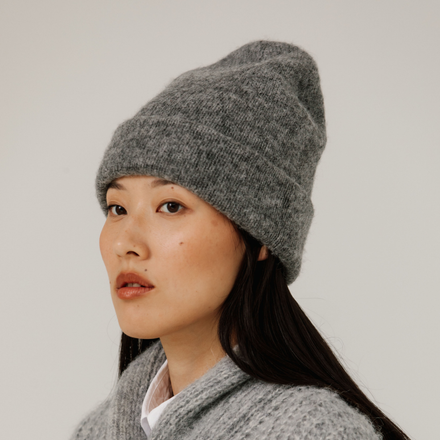 Person wearing a gray knit beanie and sweater against a plain background